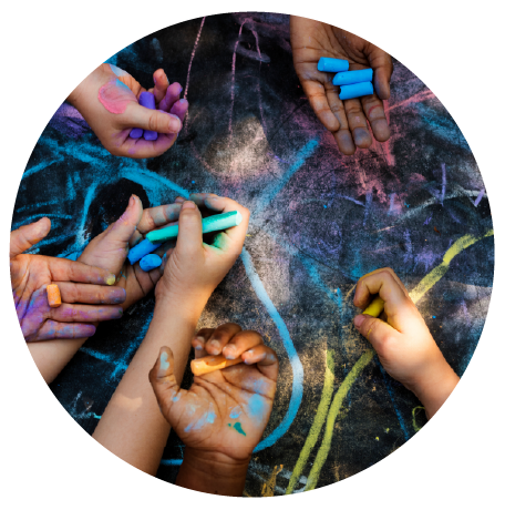 Children’s hands drawing with colorful chalk on pavement, symbolizing creativity and collaboration.