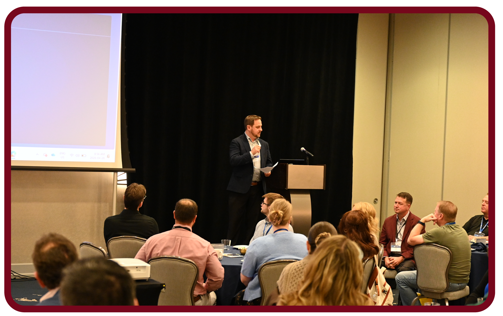 Presenter speaks at Rego University while attendees participate in a live conference session and discussion.