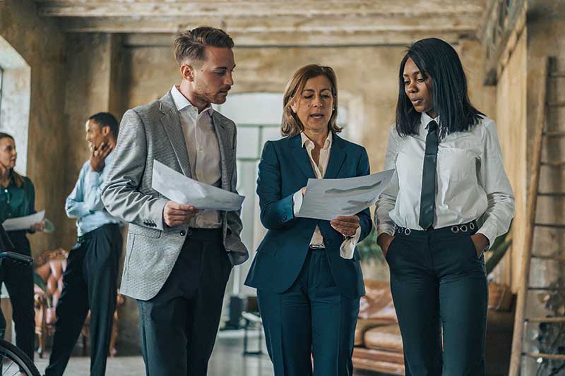 Three business professionals discuss printed documents in an office.