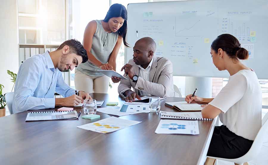 Four business professionals review charts and take notes during a team planning meeting.